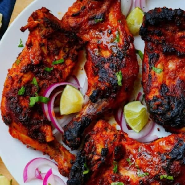 HotBits Indian Cuisine's Tandoori Chicken, garnished with red onions, lime wedges, and cilantro.