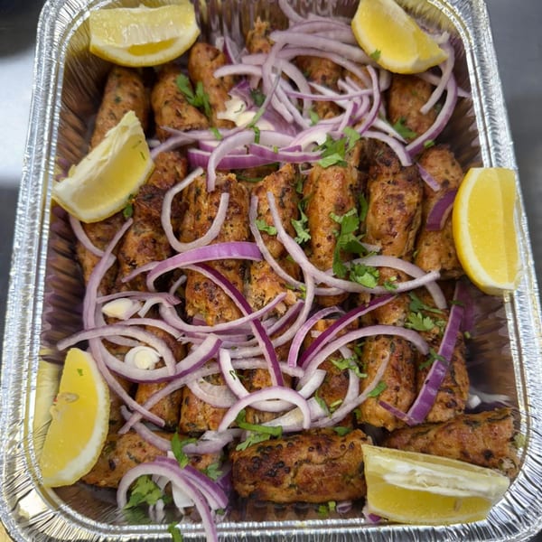 HotBits Indian Cuisine's seekh kebabs, garnished with red onion, cilantro, and lemon wedges in a foil tray.