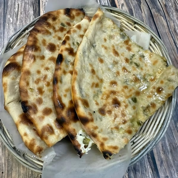 Four pieces of HotBits Indian Cuisine naan bread, some with green herbs, in a metal basket.