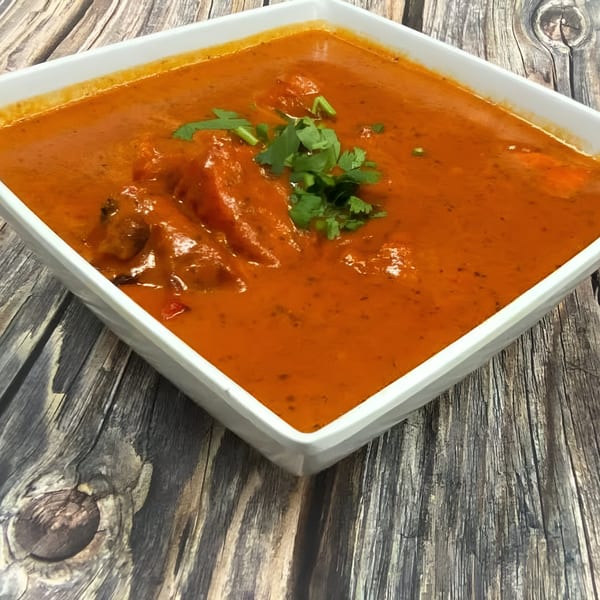 HotBits Indian Cuisine's vibrant orange butter chicken, garnished with fresh cilantro, in a white square bowl.